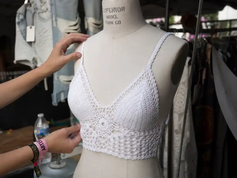 Stylist hands adjusting crochet fringe top on dress form backstage at summer music festival showing craftsmanship behind celebrity festival outfit guide women