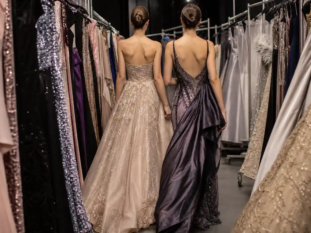 Haute couture evening gowns on rolling racks in designer showroom showing luxury construction behind celebrity gala dress inspiration atelier preparation