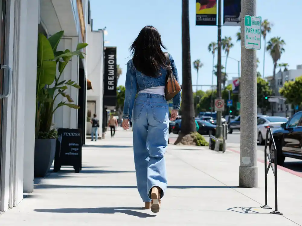 Denim off-duty celebrity inspired outfits for women with high-waisted jeans cropped top and designer bag on shopping street from behind