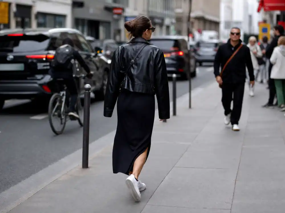 Casual celebrity inspired outfits for women with leather jacket midi skirt and sneakers on urban sidewalk showing off-duty street style recreation