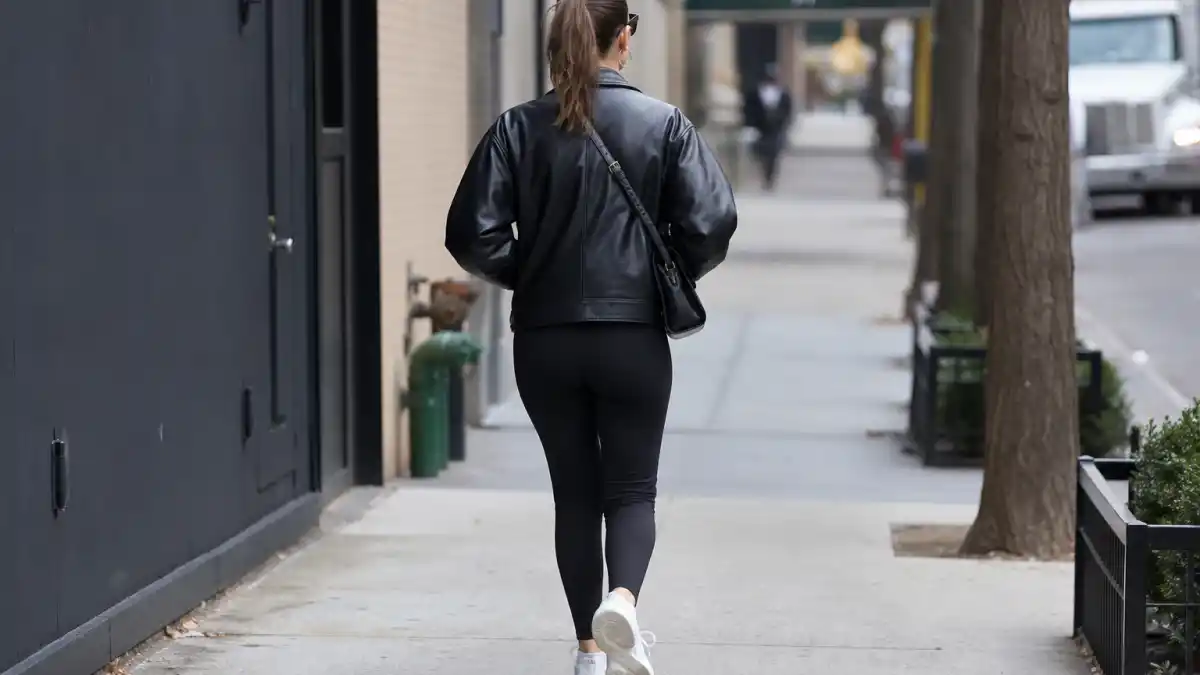 Celebrity model off duty outfits — black leather jacket black leggings white sneakers and crossbody bag on NYC sidewalk seen from behind
