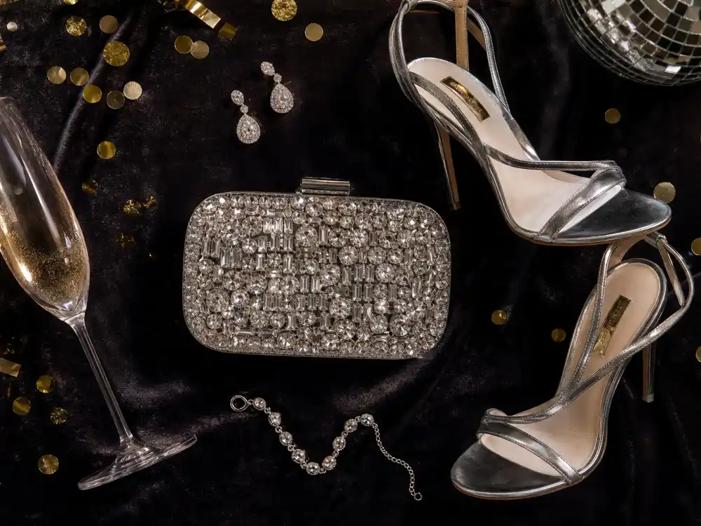 Diamond drop earrings crystal minaudiere strappy silver heels and bracelet flat lay completing accessory stacking rules for celebrity new year eve outfits 2026 champagne party finishing touches