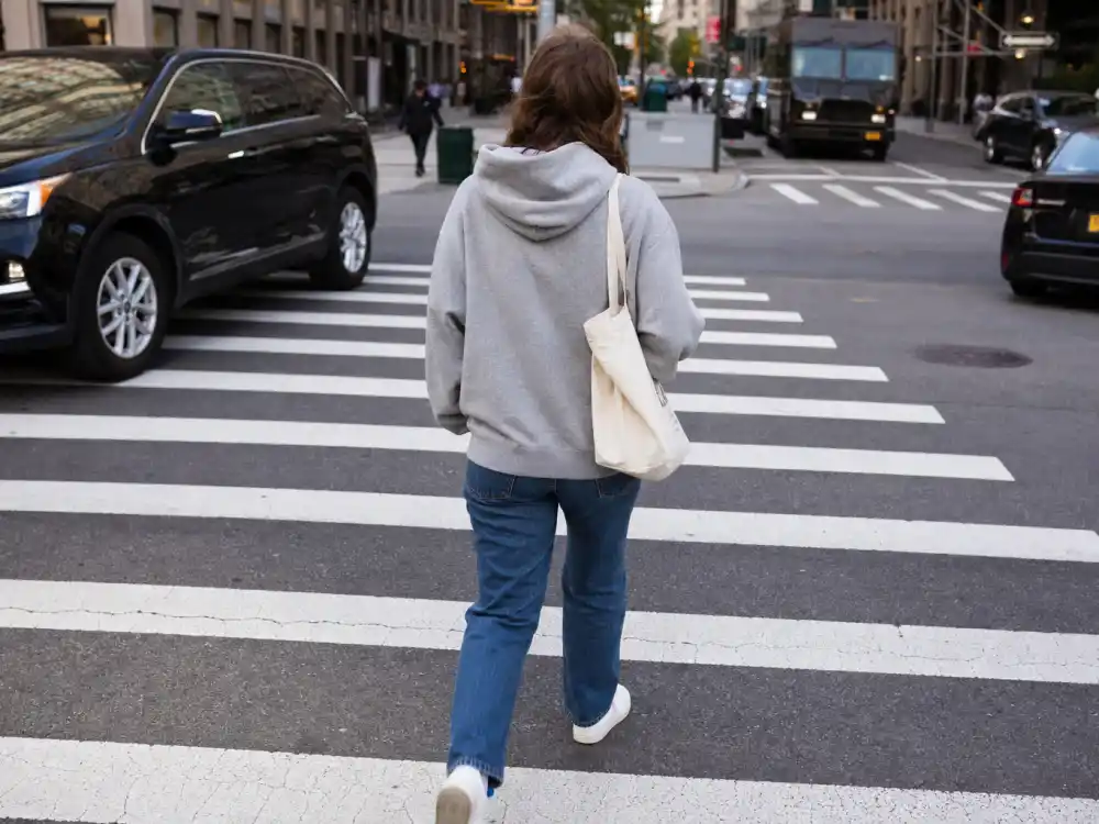 Anonymous figure from behind crossing city crosswalk in gray hoodie and jeans for celebrity normcore fashion trend paparazzi street moment