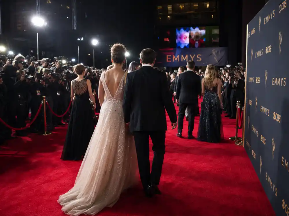 Premiere red carpet with anonymous figures from behind in evening gowns and tuxedos illustrating celebrity outfits glamour codes under paparazzi flash
