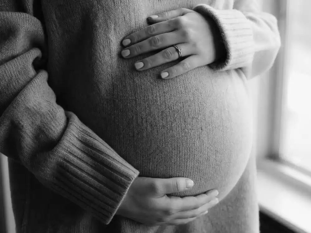 Black-and-white belly hand-grasp photo for celebrity pregnancy announcement trends 2026 — torso-only reveal without showing faces