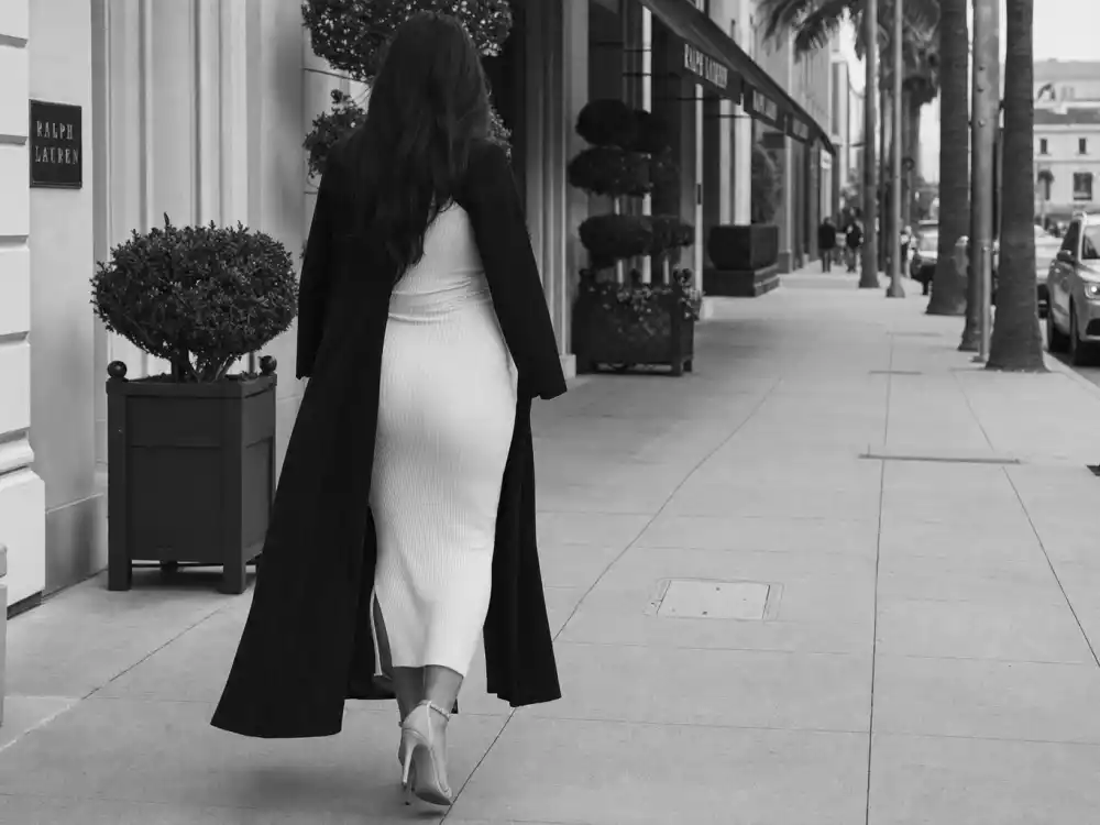 Anonymous pregnant woman in white ribbed dress and black long coat on Beverly Hills sidewalk defining celebrity pregnancy street style 2026 monochrome palette