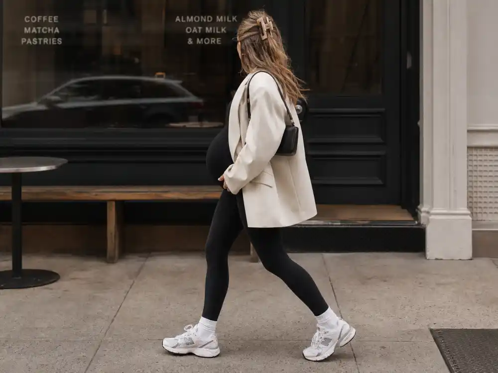 Anonymous pregnant woman in black leggings and cream blazer outside coffee shop illustrating celebrity pregnancy street style 2026 off-duty trend codes