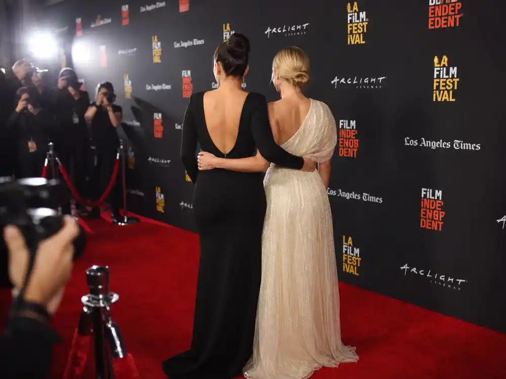 Movie premiere red carpet with step-and-repeat backdrop and anonymous figures from behind defining celebrity red carpet best dressed all time arrival moments under paparazzi flash