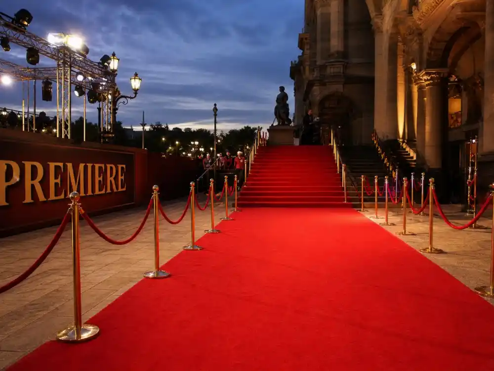 Grand theater premiere staircase with red carpet runner and velvet rope stanchions ready for celebrity red carpet best dressed all time arrivals at dusk