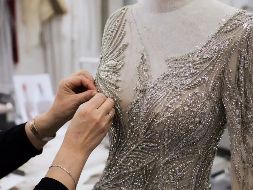 Stylist hands adjusting silver sequin beading on red carpet gown bodice showing couture construction behind celebrity red carpet dresses 2026 atelier craftsmanship