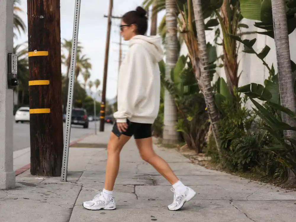 Oversized cream hoodie with black biker shorts and chunky white sneakers finishing celebrity sneaker street style outfits LA sidewalk codes