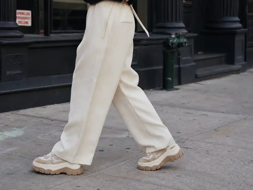 Retro chunky platform sneakers with ivory wide-leg trousers defining celebrity sneaker street style outfits proportion play on city sidewalk