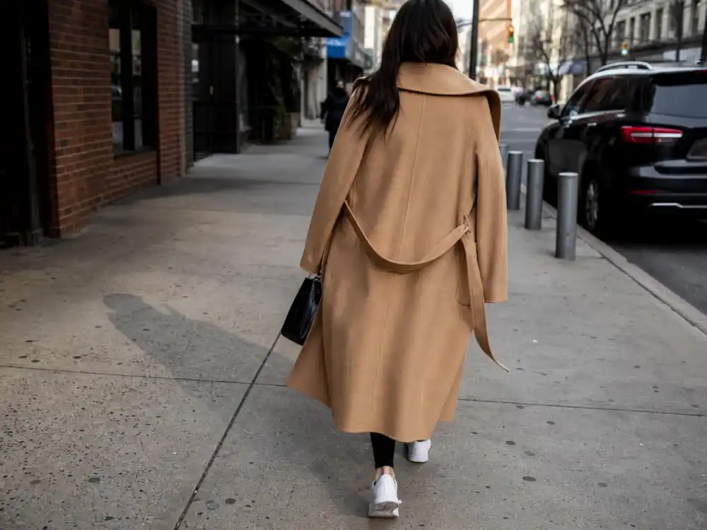 Long camel wool trench coat draped over shoulders central to celebrity street style outerwear codes on Manhattan sidewalk