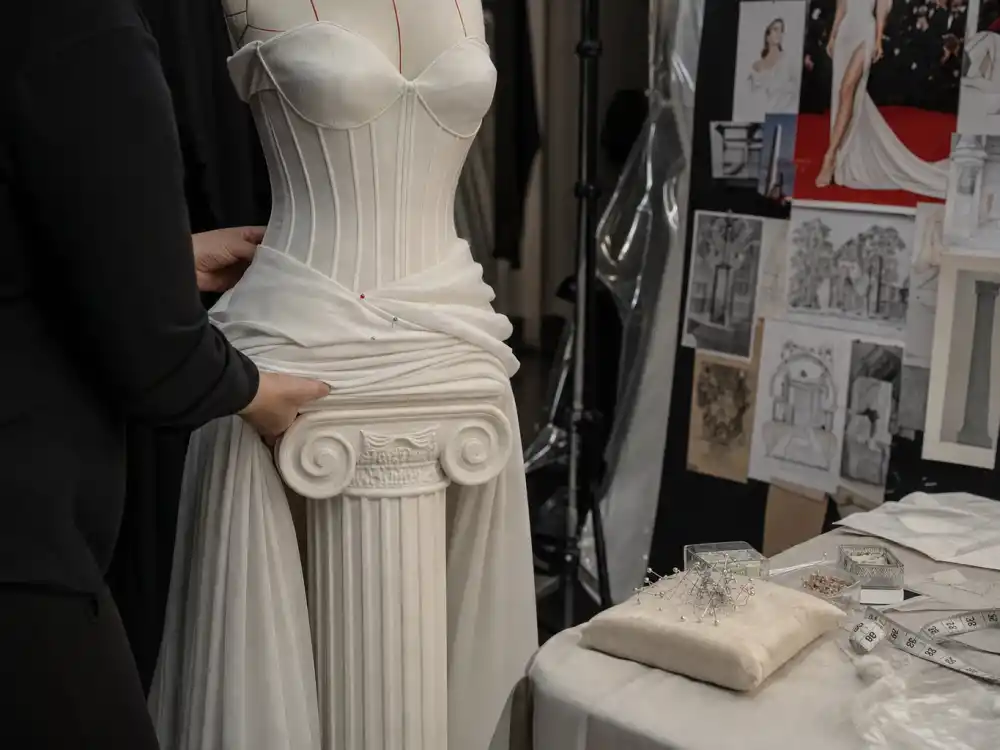 Tailor adjusting corsetry on white column gown in fitting room revealing construction steps behind how celebrity stylists pick red carpet looks before call time