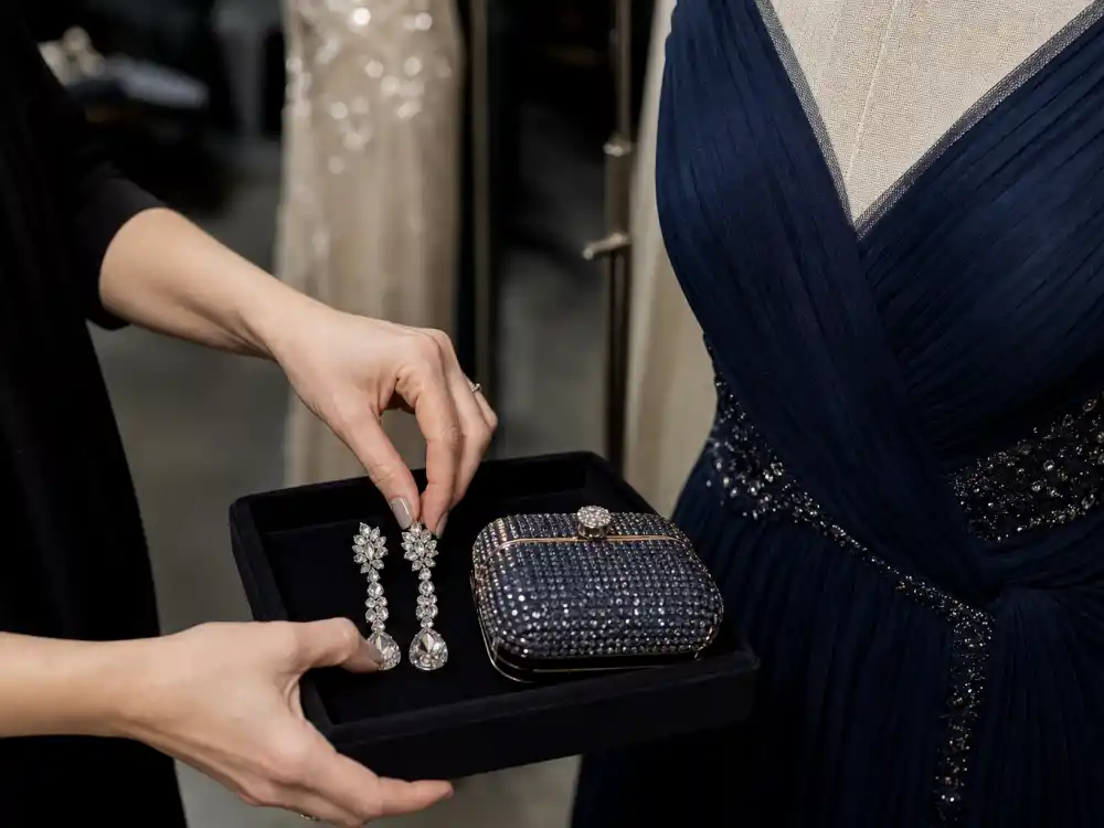 Stylist arranging crystal earrings and clutch beside navy gown on dress form showing how celebrity stylists pick red carpet looks through accessory editing