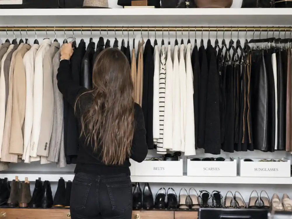 Open luxury closet with celebrity stylist wardrobe essentials including neutral blazers, cashmere sweaters, leather jackets, and ankle boots on organized hangers