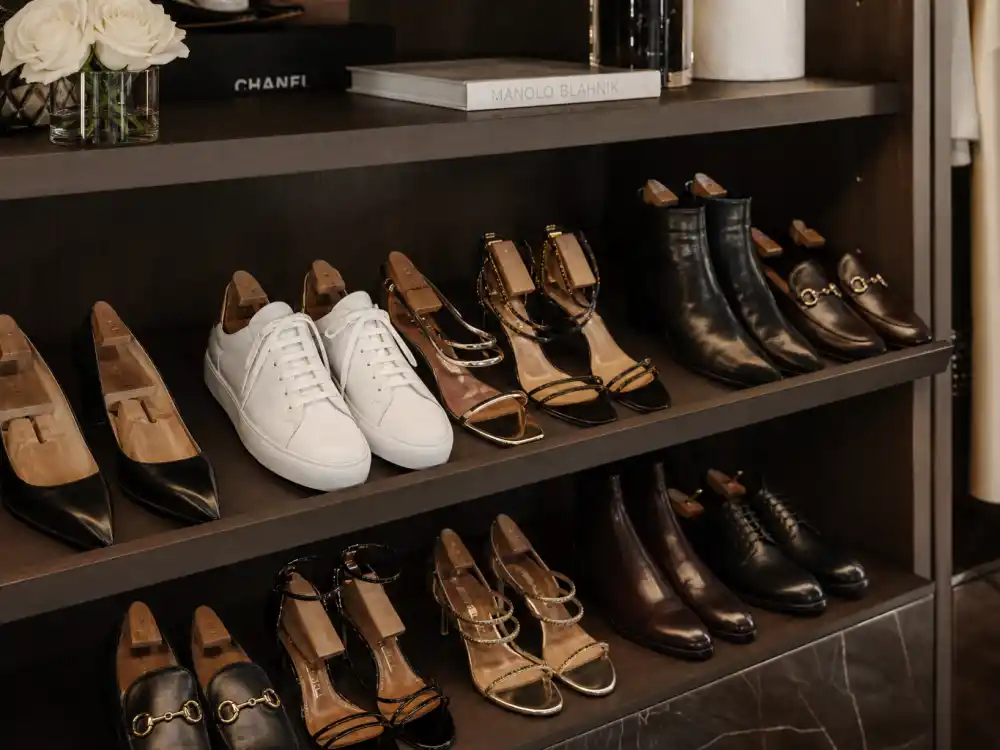 Shoe closet shelf displaying celebrity stylist wardrobe essentials including black pumps, white sneakers, strappy sandals, ankle boots, and loafers on organized shelves