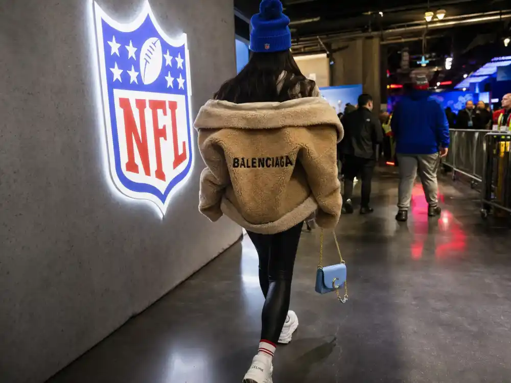 Anonymous woman from behind in shearling jacket and team-color beanie walking NFL stadium concourse for celebrity super bowl fashion 2026 arrival street style