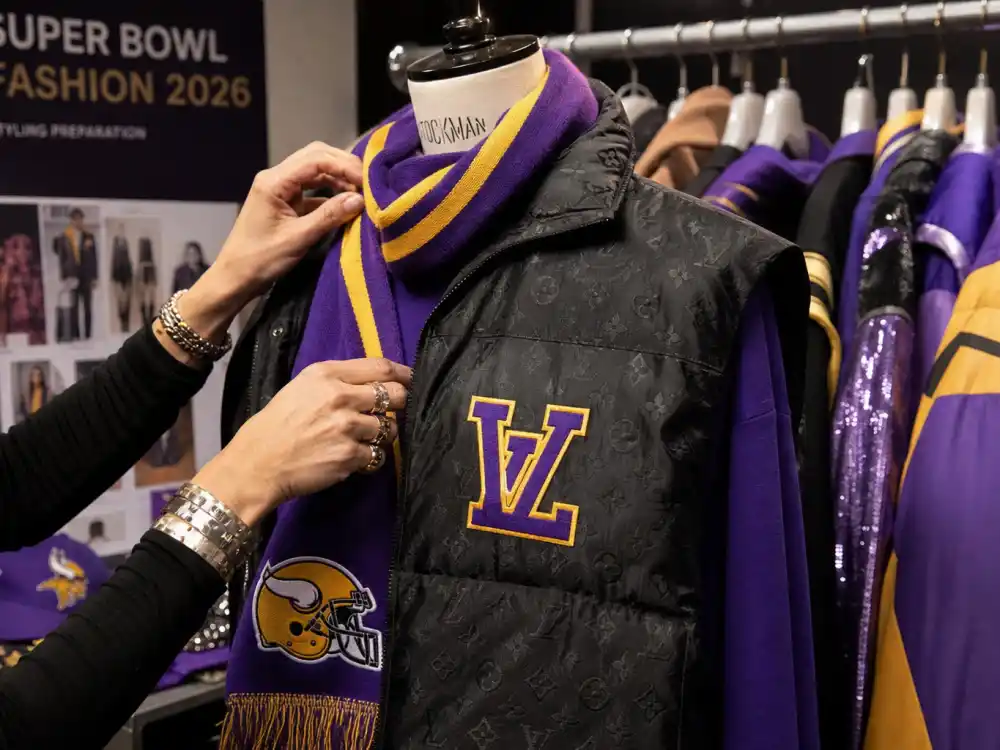 Fashion stylist hands adjusting designer puffer vest and team-color scarf on dress form backstage showing celebrity super bowl fashion 2026 preparation craft