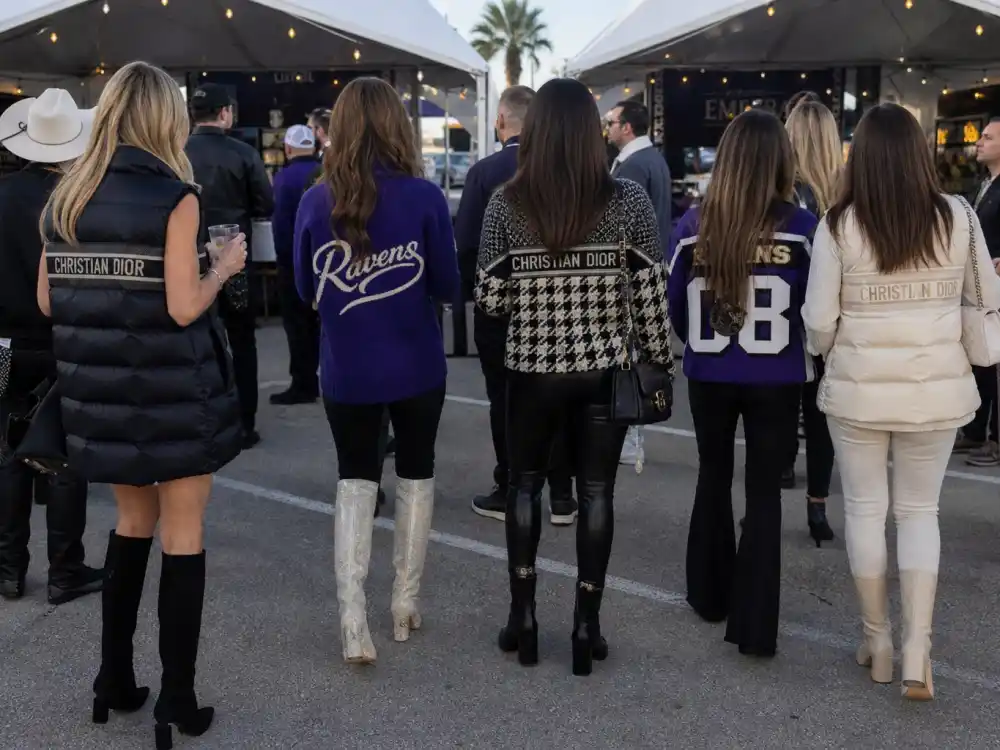 Anonymous figures from behind at upscale tailgate wearing designer puffer vests team-color knits and luxury boots illustrating celebrity super bowl fashion 2026 pregame style