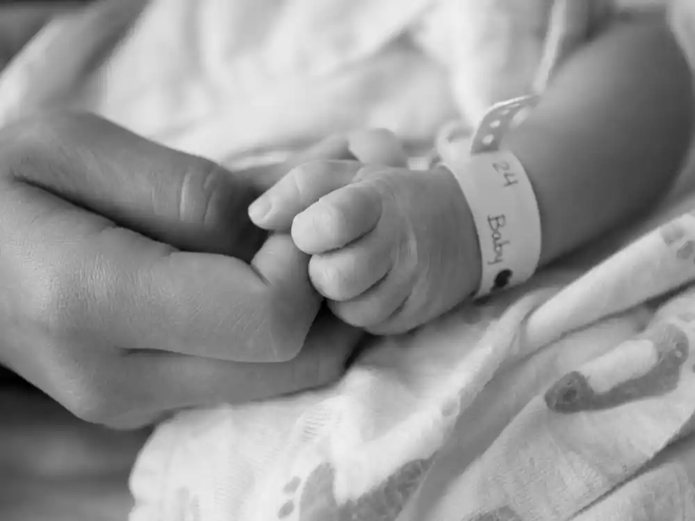 Black-and-white hand-grasp photo for celebrity surprise baby announcements 2025 — parent fingers curled around newborn without showing faces