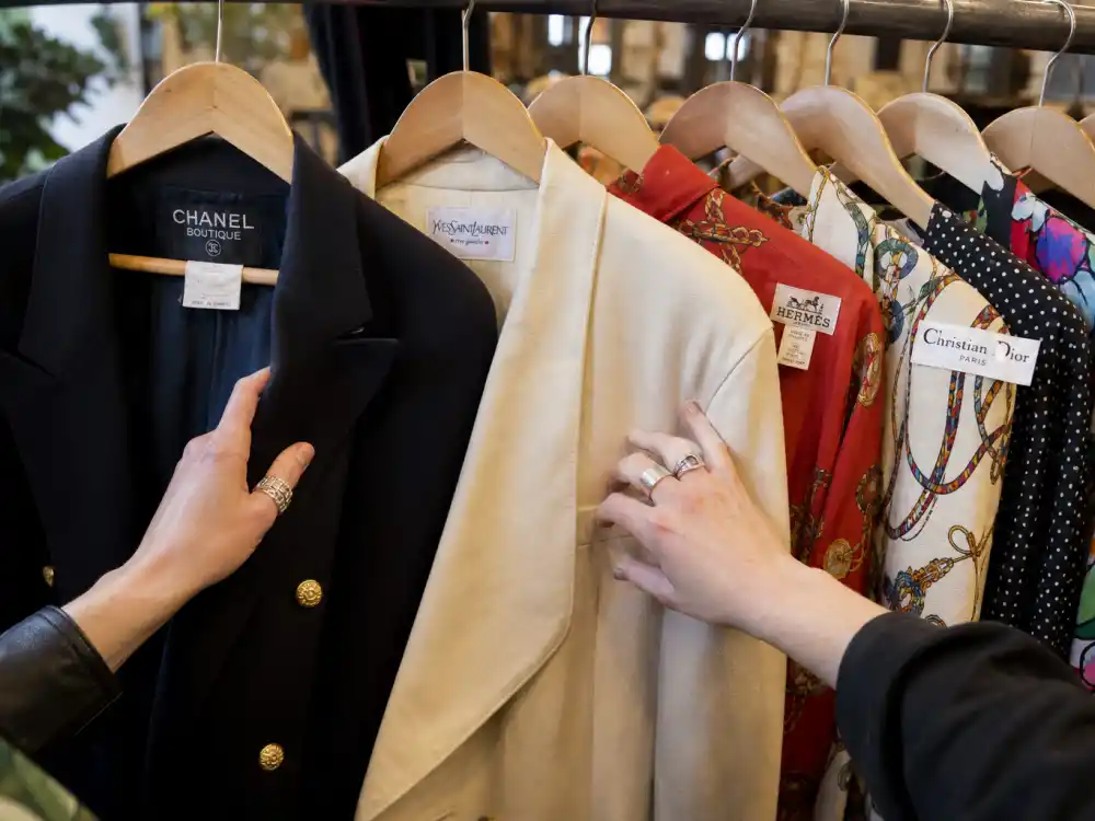 Hands browsing luxury vintage designer blazers on curated resale rack showing thrifted luxury lane within celebrity vintage designer fashion culture