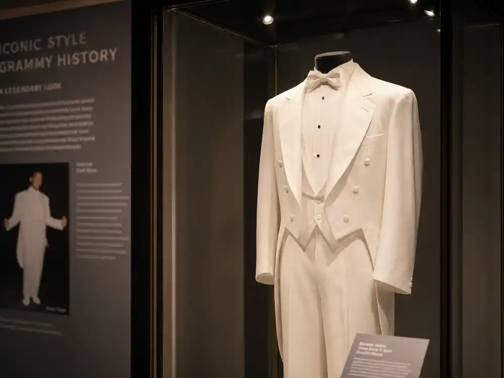 Fashion museum glass case preserving Celine Dion reverse tuxedo Grammys legacy — white backwards tailcoat on gallery mannequin under spotlight