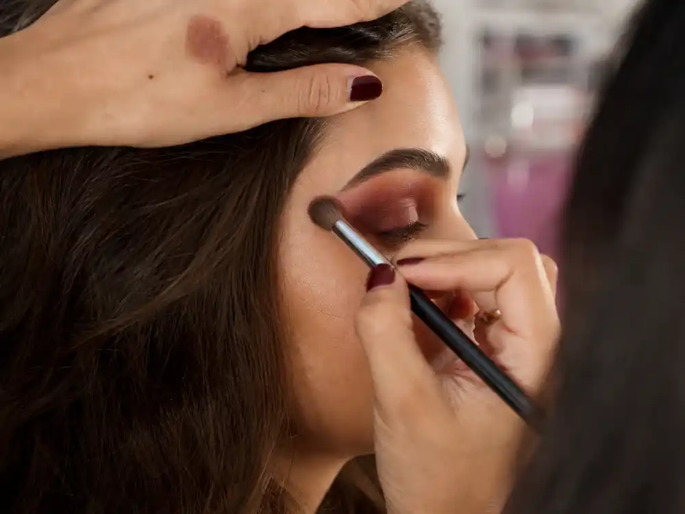 Makeup artist blending warm cherry cola eyeshadow on anonymous model eye for cherry cola beauty celebrity trend bronze-burgundy lid technique
