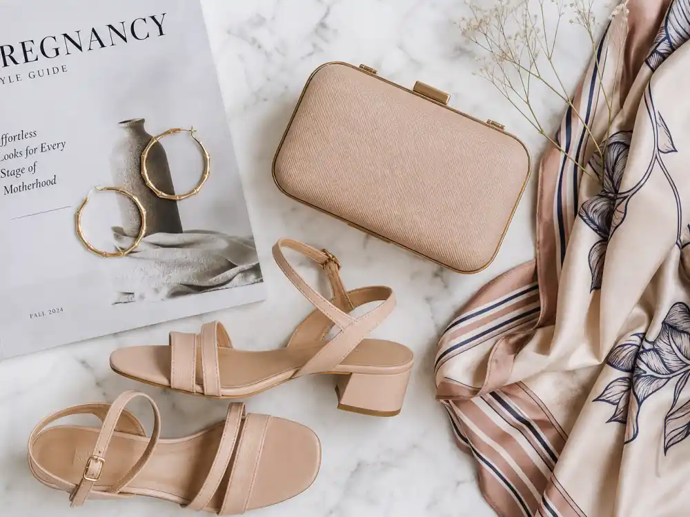Maternity fashion accessories flat lay with gold hoop earrings nude heels clutch and silk scarf completing Chrissy Teigen maternity style outfits styling vocabulary