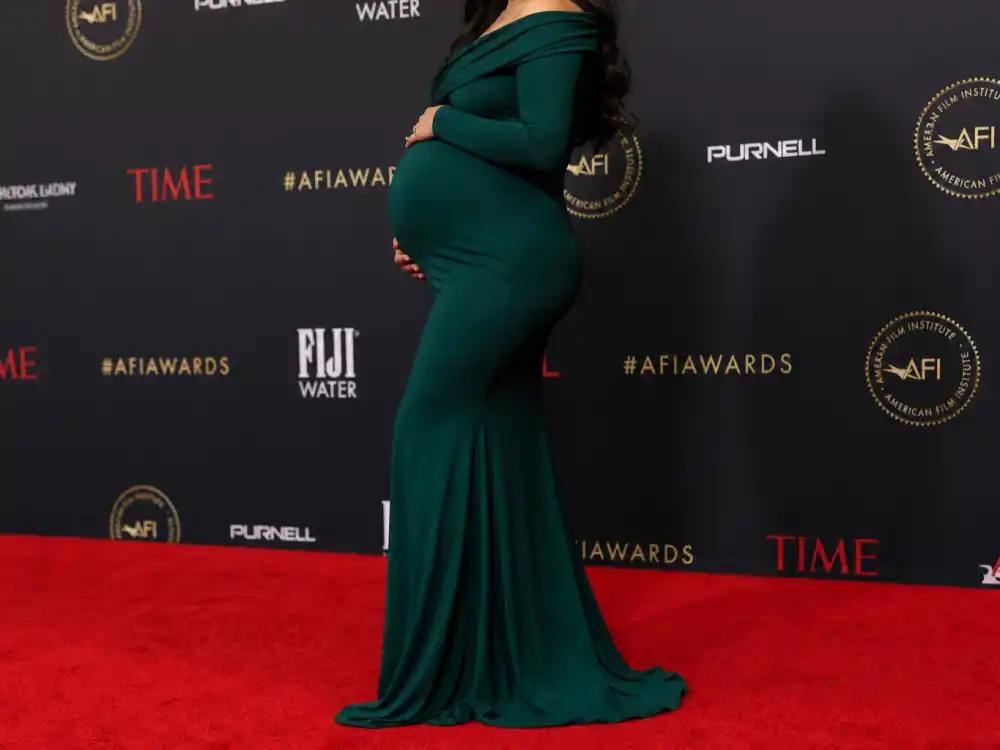 Anonymous pregnant woman in emerald green bodycon gown on red carpet step-and-repeat defining Chrissy Teigen maternity style outfits formal event dressing
