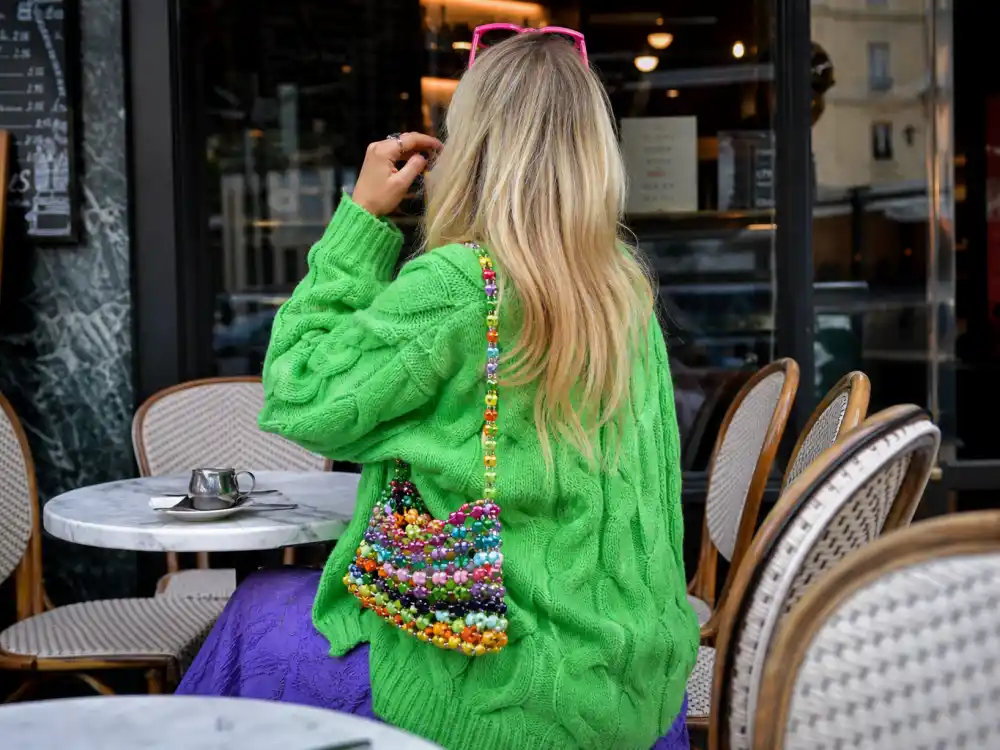 Anonymous figure from behind at outdoor cafe wearing dopamine dressing celebrity outfits layered neon green cardigan purple dress and multicolor beaded bag