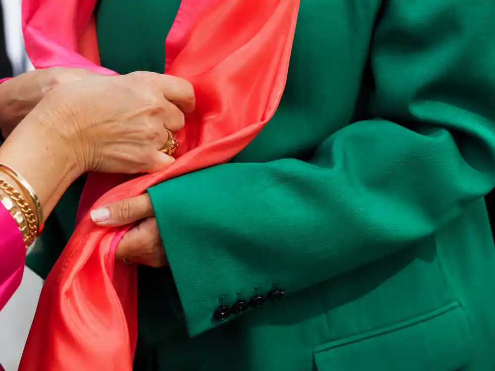 Hands adjusting coral satin scarf over emerald green blazer sleeve defining dopamine dressing celebrity outfits bold color styling detail