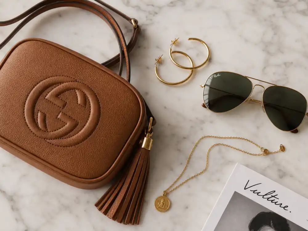 Tan crossbody bag aviator sunglasses and gold hoops finishing Gigi Hadid street style 2026 accessory layer