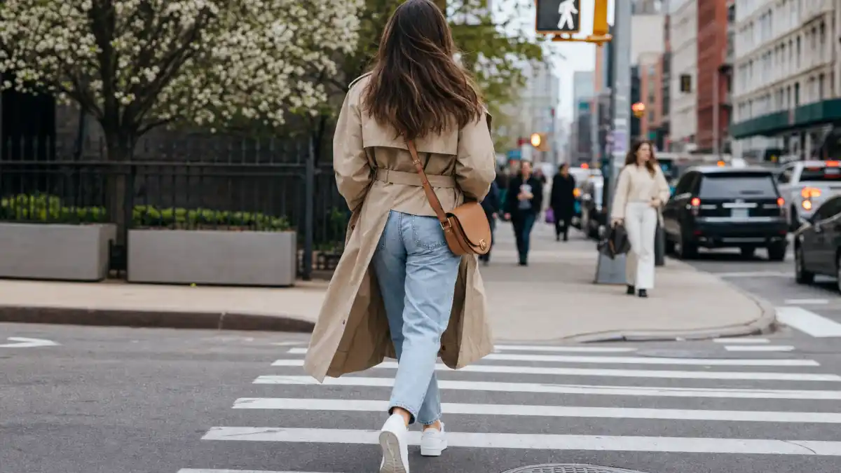 Gigi Hadid street style 2026 — camel trench coat mom jeans white sneakers and crossbody bag on NYC sidewalk seen from behind