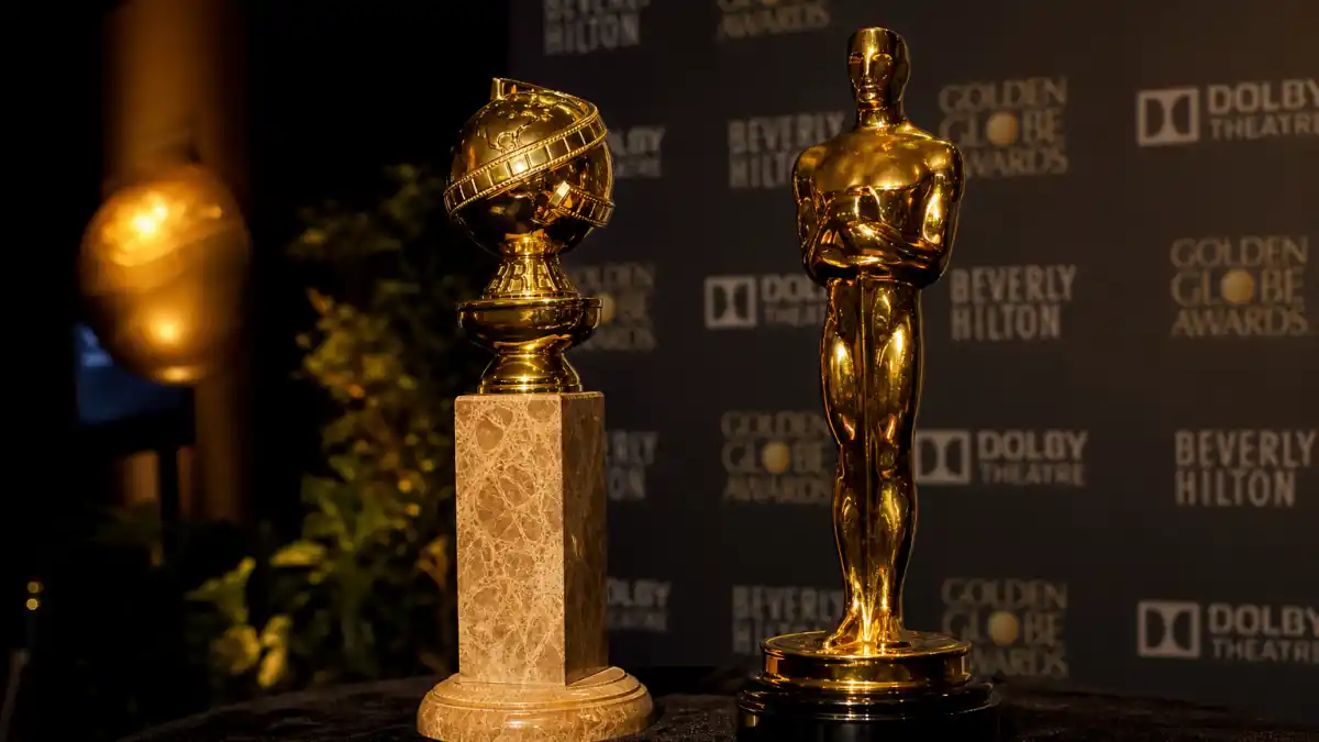 Golden Globes vs Oscars difference explained — Golden Globe and Oscar statuettes side by side at Beverly Hilton and Dolby Theatre press wall