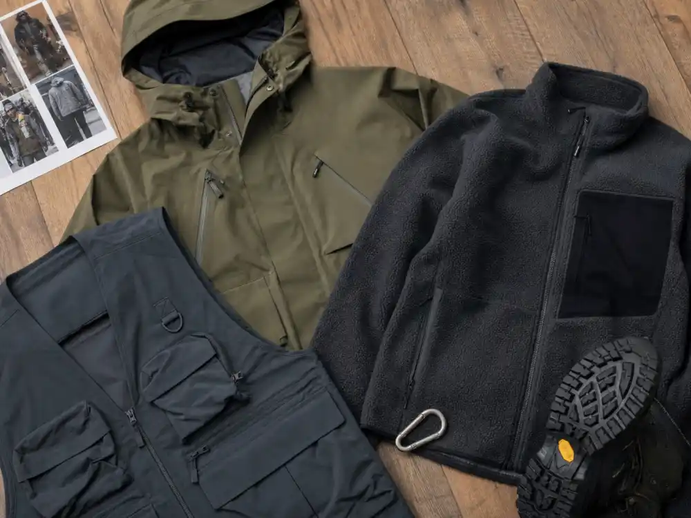 Flat lay of technical shell jacket, fleece midlayer, and utility vest defining gorpcore celebrity street style outerwear layering codes