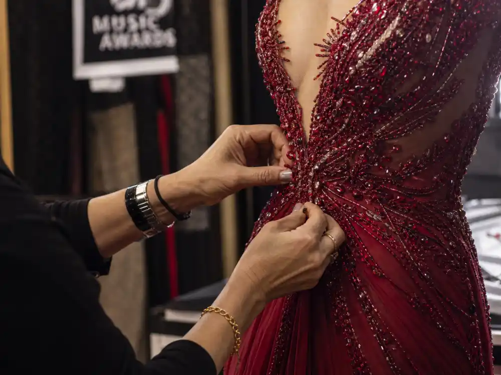 Stylist hands adjusting crystal beading on red carpet evening gown bodice showing couture construction behind grammy awards celebrity outfits 2026 atelier craftsmanship
