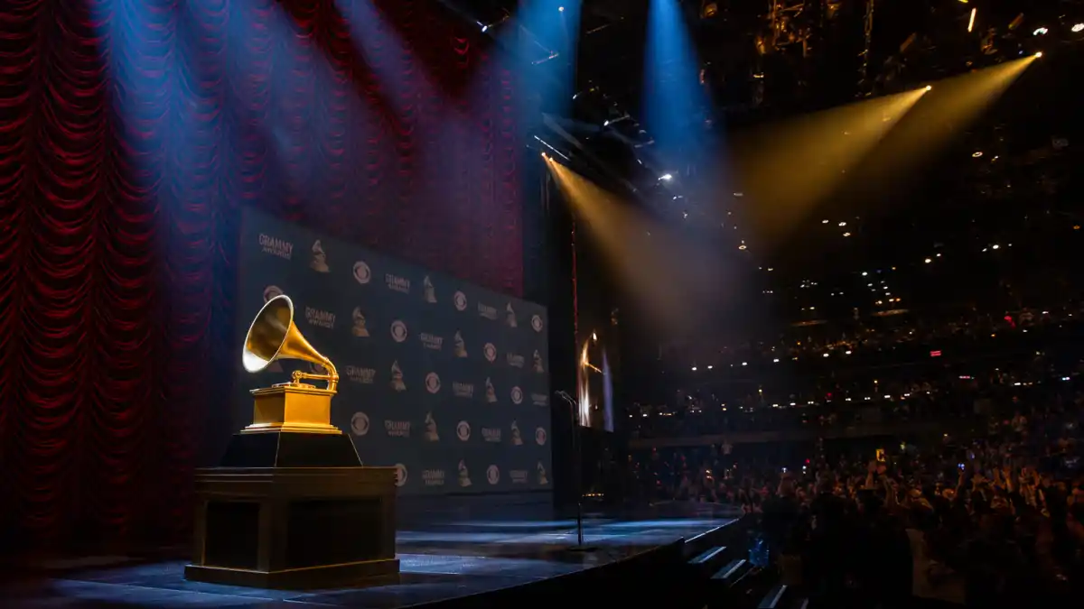 Grammys most shocking moments history — dramatic awards theatre stage with golden trophy silhouette and shocked audience silhouettes under spotlights