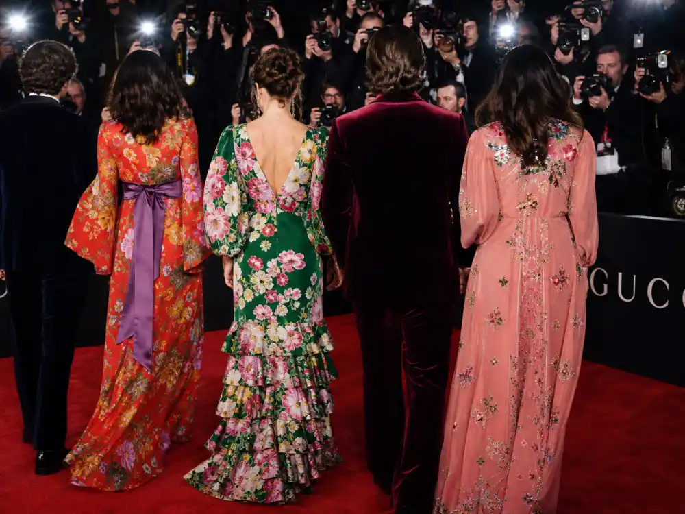 Step-and-repeat premiere with anonymous figures in bold floral Gucci gowns illustrating Gucci celebrity red carpet style at awards season flash points