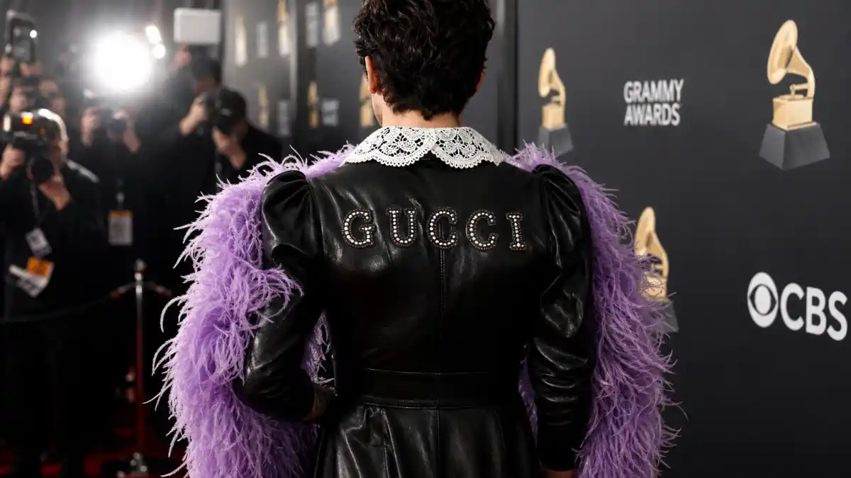Harry Styles Gucci dress Grammy history — custom black leather gown with white lace Peter Pan collar and purple feather boa photographed from behind on 63rd Grammy Awards red carpet