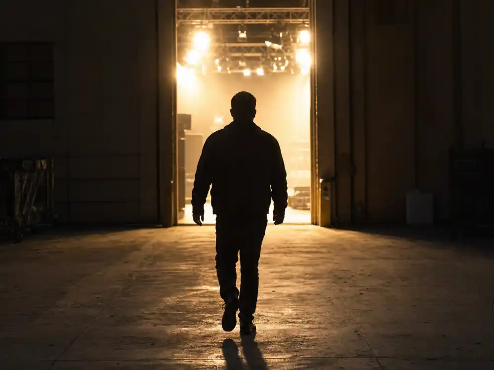 A silhouette walking toward a lit studio stage door, showing where Hayden Christensen is now in 2026
