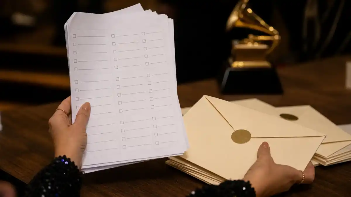 How are Grammy winners chosen — blank voting ballots and sealed envelopes beside a golden gramophone trophy under warm backstage light