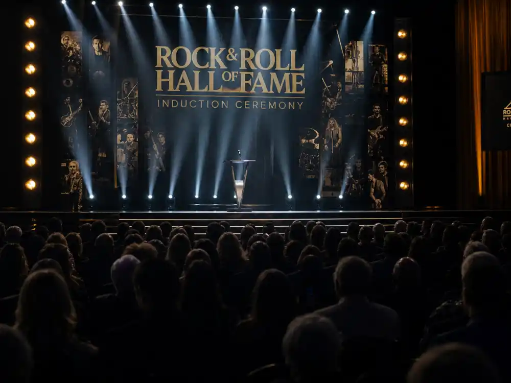 Rock Hall induction ceremony stage for how are Rock Hall inductees chosen — anonymous audience silhouettes watching spotlight podium reveal