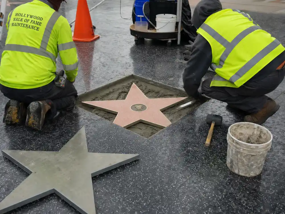 Workers installing a bronze Hollywood Walk of Fame star into terrazzo sidewalk during how do celebrities get a Hollywood Walk of Fame star unveiling ceremony prep