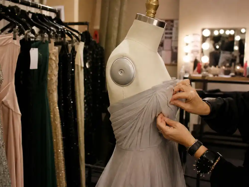 Celebrity stylist pinning formal gown on dress form for how do celebrities prepare for award shows — racks of evening wear in backstage dressing room