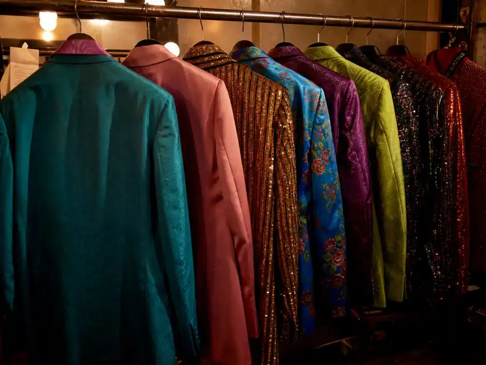 Flamboyant colorful suits on clothing rack from behind reflecting how old is Harry Styles fashion-forward solo era and red-carpet style evolution