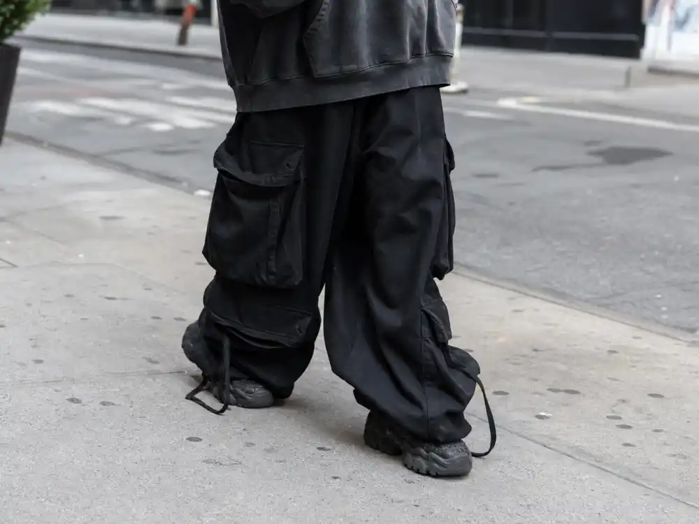 Extremely baggy black cargo pants pooling over sneakers defining how to dress like Billie Eilish oversized style anti-fit bottoms
