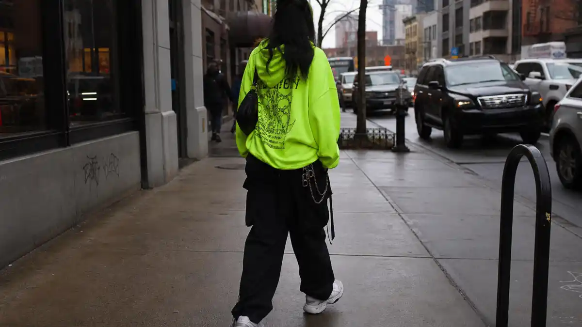 How to dress like Billie Eilish oversized style — neon green hoodie baggy cargo pants chunky sneakers and silver chains on urban sidewalk seen from behind