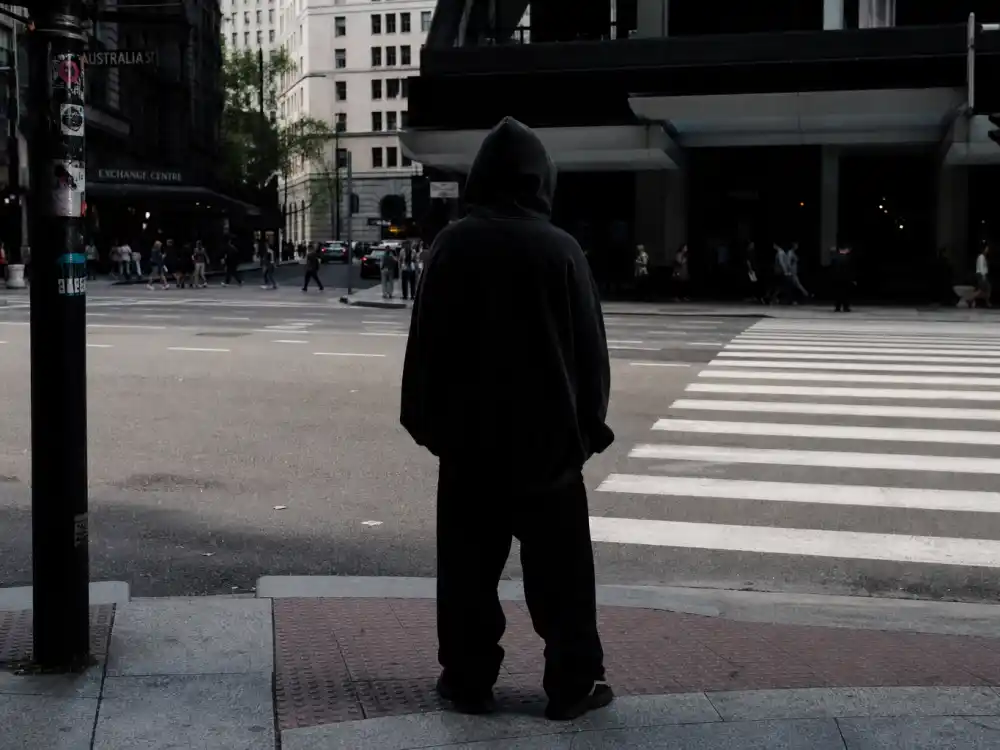 Urban crosswalk silhouette in massive hoodie and baggy pants behind how to dress like Billie Eilish oversized style sidewalk energy