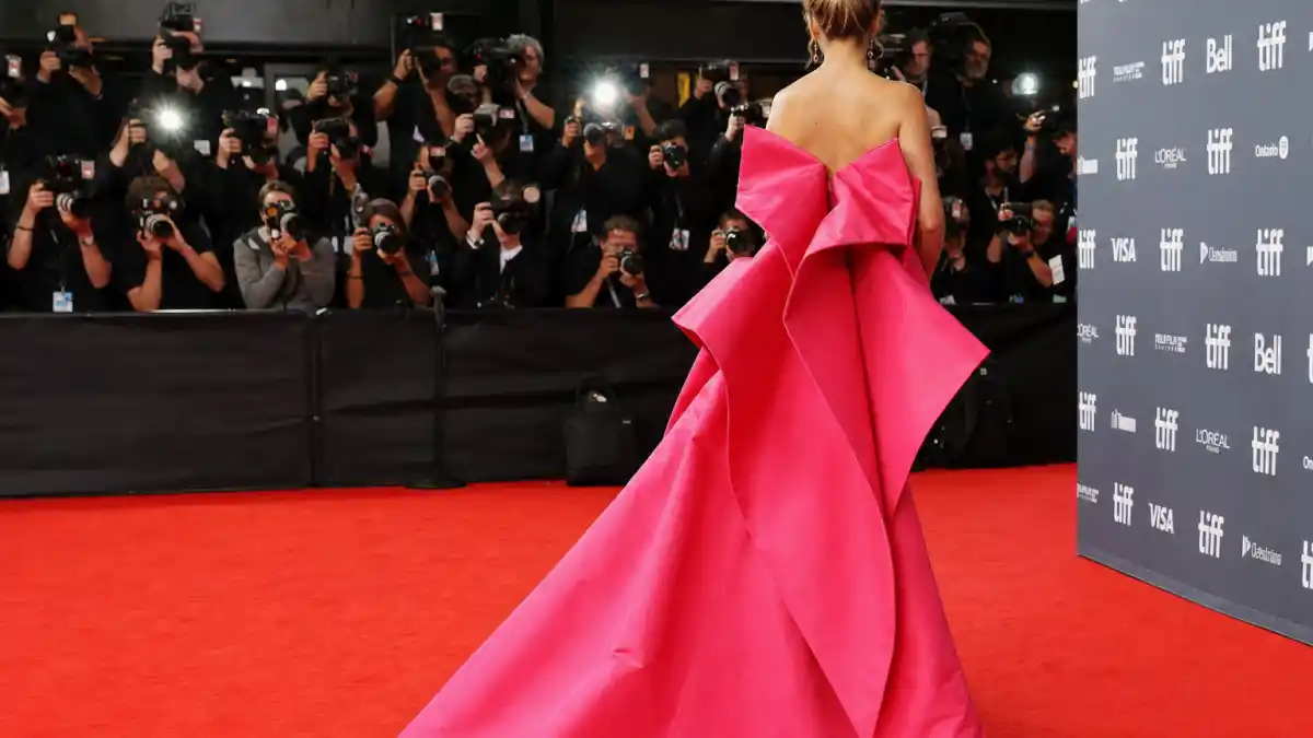 How to dress like Florence Pugh red carpet bold — hot pink structural gown on premiere red carpet seen from behind with photographers and step-and-repeat backdrop